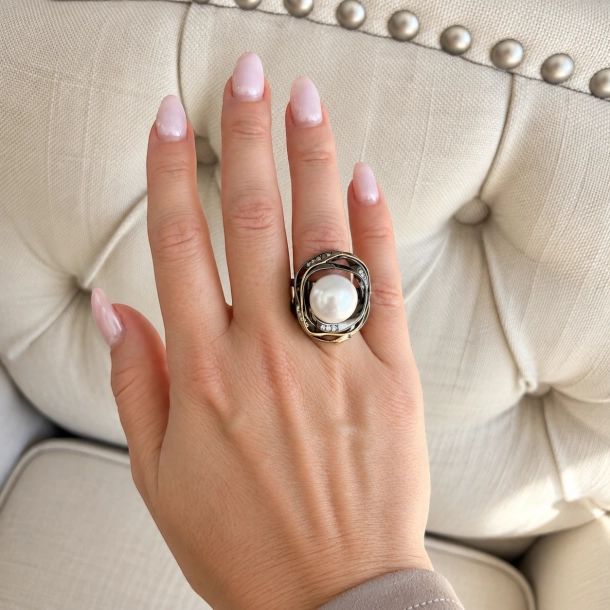 Stor hvid ferskvandsperle b�ret p� pegefinger — m�rkt rhodium m�der 18k guld i et snoet fat med topasstene.